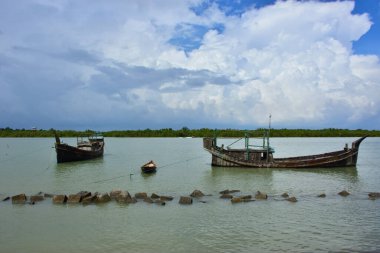 Bangladeş 'teki engin bir nehrin geniş açılı görüntüsü dramatik, bulutlu bir gökyüzü altında. Karanlık bulutlar muson mevsiminde sakin su üzerinde güçlü bir atmosfer yaratırlar..