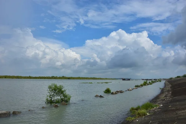 Mavi gökyüzüne karşı parlak beyaz kümülüs bulutlarının yer aldığı güzel bir sahil su yolu. Bangladeş kırsalında temiz su ve yemyeşil alan mükemmel bir yaz gününü yakalıyor..