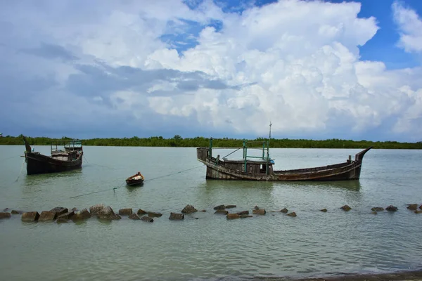 Bangladeş 'teki engin bir nehrin geniş açılı görüntüsü dramatik, bulutlu bir gökyüzü altında. Karanlık bulutlar muson mevsiminde sakin su üzerinde güçlü bir atmosfer yaratırlar..