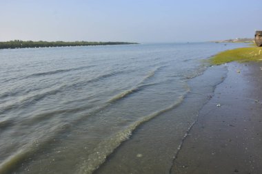 Bakkhali Nehri 'nin sakin bir uzantısı, sığ bir kıyı şeridi boyunca hafif dalgalanmalarla, Bangladeş, Coxs Bazar' da huzurlu bir gelgit nehri manzarasını gösteriyor..