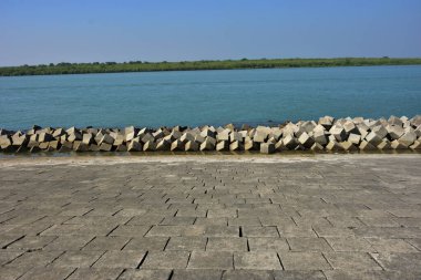 Berrak mavi gökyüzünün altındaki sakin nehir suyu boyunca beton set geçidi. Güçlü perspektif çizgileri olan barışçıl açık hava manzarası, seyahat, altyapı, kentsel planlama, doğa ve çevre kavramları için uygundur..