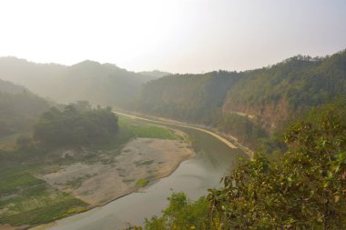 Matamuhuri Nehri 'nin geniş açılı manzarası Lama, Bandarban ve Bangladeş tepelerinden geçiyor. S-eğrisi, kumlu bankalar ve yemyeşil tropikal bitki örtüsü. Sıcak öğleden sonra ışığıyla vadinin üzerinde yumuşak bir sis var. Bangladeş 'in Yeşil Çatı.