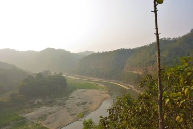 Matamuhuri Nehri 'nin geniş açılı manzarası Lama, Bandarban ve Bangladeş tepelerinden geçiyor. S-eğrisi, kumlu bankalar ve yemyeşil tropikal bitki örtüsü. Sıcak öğleden sonra ışığıyla vadinin üzerinde yumuşak bir sis var. Bangladeş 'in Yeşil Çatı.