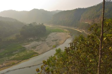 Matamuhuri Nehri 'nin geniş açılı manzarası Lama, Bandarban ve Bangladeş tepelerinden geçiyor. S-eğrisi, kumlu bankalar ve yemyeşil tropikal bitki örtüsü. Sıcak öğleden sonra ışığıyla vadinin üzerinde yumuşak bir sis var. Bangladeş 'in Yeşil Çatı.
