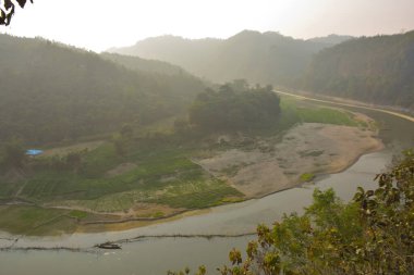 Matamuhuri Nehri 'nin geniş açılı manzarası Lama, Bandarban ve Bangladeş tepelerinden geçiyor. S-eğrisi, kumlu bankalar ve yemyeşil tropikal bitki örtüsü. Sıcak öğleden sonra ışığıyla vadinin üzerinde yumuşak bir sis var. Bangladeş 'in Yeşil Çatı.