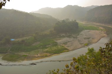 Matamuhuri Nehri 'nin geniş açılı manzarası Lama, Bandarban ve Bangladeş tepelerinden geçiyor. S-eğrisi, kumlu bankalar ve yemyeşil tropikal bitki örtüsü. Sıcak öğleden sonra ışığıyla vadinin üzerinde yumuşak bir sis var. Bangladeş 'in Yeşil Çatı.