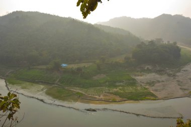 Matamuhuri Nehri 'nin geniş açılı manzarası Lama, Bandarban ve Bangladeş tepelerinden geçiyor. S-eğrisi, kumlu bankalar ve yemyeşil tropikal bitki örtüsü. Sıcak öğleden sonra ışığıyla vadinin üzerinde yumuşak bir sis var. Bangladeş 'in Yeşil Çatı.