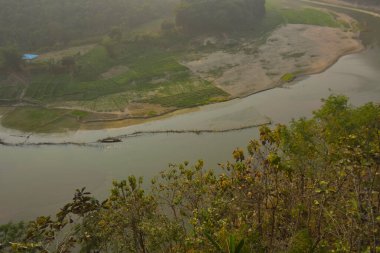 Matamuhuri Nehri 'nin geniş açılı manzarası Lama, Bandarban ve Bangladeş tepelerinden geçiyor. S-eğrisi, kumlu bankalar ve yemyeşil tropikal bitki örtüsü. Sıcak öğleden sonra ışığıyla vadinin üzerinde yumuşak bir sis var. Bangladeş 'in Yeşil Çatı.