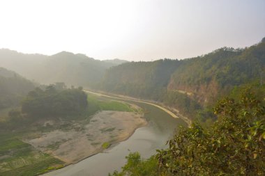 Matamuhuri Nehri 'nin geniş açılı manzarası Lama, Bandarban ve Bangladeş tepelerinden geçiyor. S-eğrisi, kumlu bankalar ve yemyeşil tropikal bitki örtüsü. Sıcak öğleden sonra ışığıyla vadinin üzerinde yumuşak bir sis var. Bangladeş 'in Yeşil Çatı.