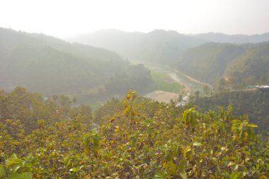 Matamuhuri Nehri (Segun) ve Bangladeş, Bandarban, Lama tepelerindeki karışık ağaç çiftliklerinin yanında. Kurak mevsim manzarası, akan nehir hatları, katmanlı tepeler, tropikal ormanlar ve sakin kırsal atmosfer..