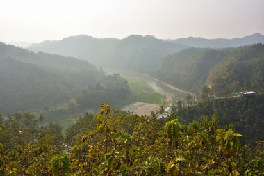 Matamuhuri Nehri 'nin Lama, Bandarban, Bangladeş tepelerindeki meşe ve karışık ağaç plantasyonlarının yanında akan manzarası, kurak mevsimde çekilmiş, sakin ışık, dış hatlar ve kırsal sükunet yakalanmıştır..