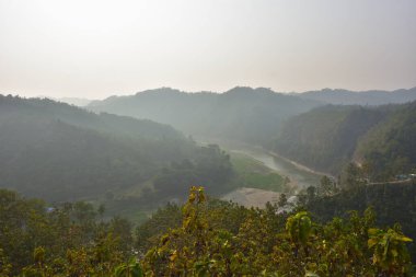 Matamuhuri Nehri 'nin Lama, Bandarban, Bangladeş tepelerindeki meşe ve karışık ağaç plantasyonlarının yanında akan manzarası, kurak mevsimde çekilmiş, sakin ışık, dış hatlar ve kırsal sükunet yakalanmıştır..