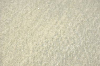 Rüzgâr ve sığ suların oluşturduğu doğal kum dalgalanmaları plaj yüzeyinde soyut desenler oluşturur. Tasarım ve doğa kavramları için ideal minimum kıyı arkaplanı, ince ışık ve organik kumlu detaylar.