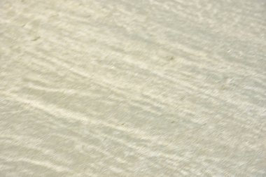 Rüzgâr ve sığ suların oluşturduğu doğal kum dalgalanmaları plaj yüzeyinde soyut desenler oluşturur. Tasarım ve doğa kavramları için ideal minimum kıyı arkaplanı, ince ışık ve organik kumlu detaylar.