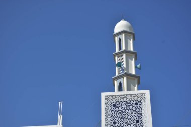 Zarif geometrik desenlere sahip modern beyaz cami minaresi açık mavi gökyüzüne karşı yükseliyor. Dini, kültürel ve barışçıl konsept betimlemeleri için ideal inanç, maneviyat ve Ramazan 'ı sembolize eden minimum İslami mimari.
