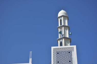 Zarif geometrik desenlere sahip modern beyaz cami minaresi açık mavi gökyüzüne karşı yükseliyor. Dini, kültürel ve barışçıl konsept betimlemeleri için ideal inanç, maneviyat ve Ramazan 'ı sembolize eden minimum İslami mimari.