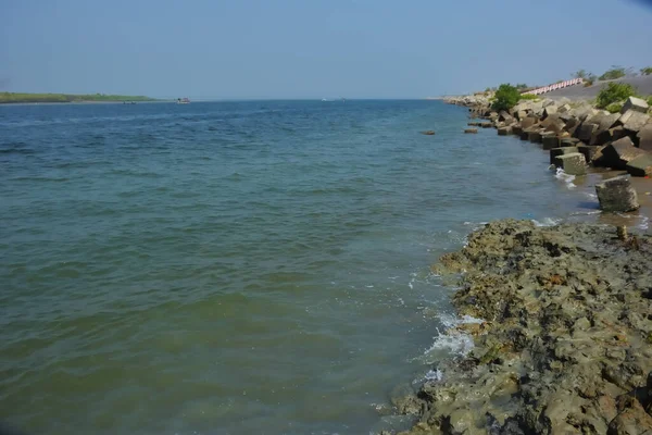 Bangladeş kıyıları boyunca kayalık bir kıyı şeridine dokunan küçük gelgit dalgaları, kıyı dokusunu, yumuşak su hareketlerini ve tropikal haliçsel bir çevredeki doğal kıyı dinamiklerini gösteriyor..