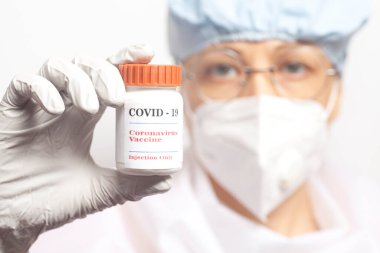 Kadın doktorun elinde bir şişe Covid-19 aşısı var. Steril giysiler içindeki bilim adamı covid-19 aşısı yapıyor..