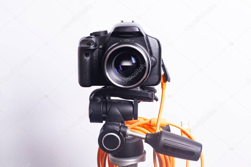 Digital photo camera on black tripod with orange cable.