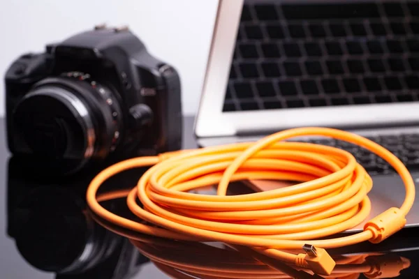 Digital photo camera connected to laptop with USB orange rolled cable.