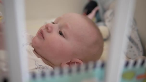 Retrato de un bebé recién nacido. El niño yace en la cuna y juega con juguetes. Muy lindos ojos. Primer plano. Movimiento lento — Vídeos de Stock