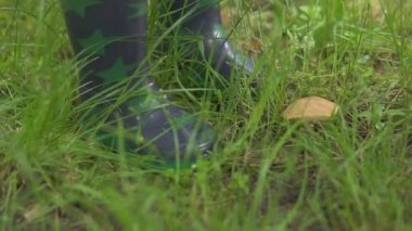 Yakından bakınca, yıldızlı gri lastik çizmeli küçük bir çocuğun ayakları küçük bir mantarın önünde duruyor.