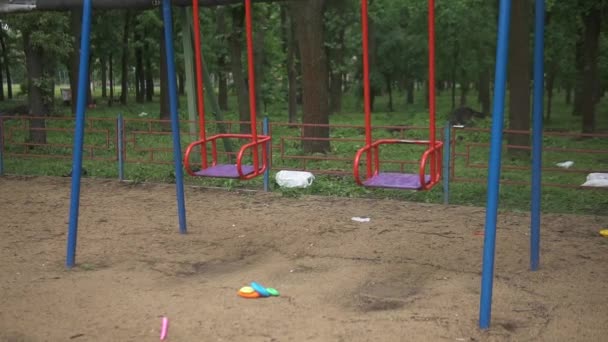 Solitario balanceo abandonado vacío rojo en un viejo parque de atracciones abandonado. Asiento oscilante moviéndose hacia adelante y hacia atrás. El carrusel se mueve lentamente. Concepto de soledad o secuestro de niños. Zona peligrosa.Ciudad fantasma. — Vídeo de stock