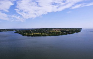 Parlak mavi gökyüzünün altında sakin sularla çevrili canlı yeşillikle çevrili doğal güzellik ve huzurun özünü yakalayan bir adanın manzarası.