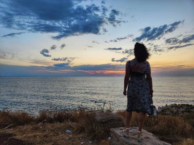 Kız gün batımında denize bakıyor.