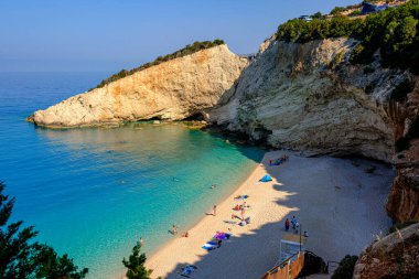 Yunanistan 'ın Lefkada kentindeki Porto Katsiki' de turkuaz su, dik kayalık uçurumlar ve güneşli bir yaz gününün keyfini çıkaran güneşli bir sahil manzarası. Manzara, İyon kıyı şeridinin doğal güzelliğini vurgular..