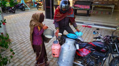 21 Ocak 2021 Badhal, Jaipur, Hindistan. Hintli bir kadın sütçüye süt döküyor. Sütçü, sütü Liter bastonuyla ölçüyor..