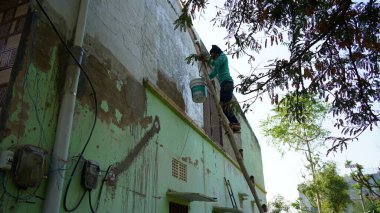 05 February 2021- Khatoo, Jaipur, India. Male painter using roller for refurbishing color of wall outdoors. Indian man decorating the walls.