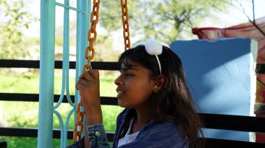 Bahçede oturan ve demir zincir sallayan güzel kızın yan görüntüsü. Kız huzurlu bir zihinle düşünüyor ve doğa huzurunun tadını çıkarıyor..