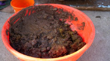 Wet Cow manure and clay mortar in a plastic tub to make a clay stove. Wet mixed cow dung or black clay manure mortar closeup. clipart