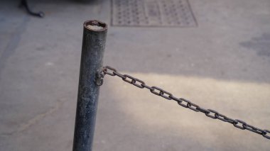 Demir bir sütun ve bağlı bir zincirden yapılmış dekoratif bir çitin ön çekimi. Yasak otomobillerin ilerlemesi için zincir görünümü.
