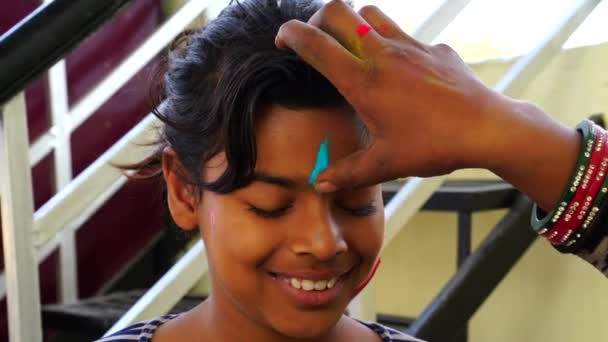 Human hand marking Gulal Tilak on little girl forehead. Girl celebrating color festival in India. Holi special 2021 concept. — Stock Video