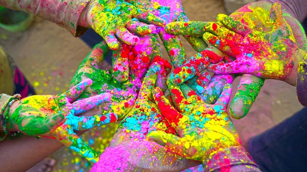 Friends hands close up in holi paint. Shine colors on fingers with Gulaal or Abhir colors. Holi festival concept.