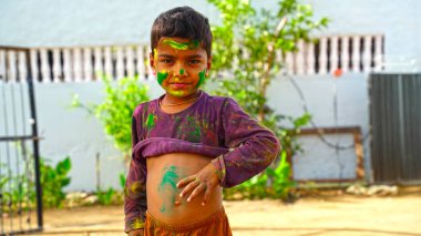 Küçük çocukla kızarmış boya tozu. Neşeli çocuk Gulaal 'ı yüzüne bulaştırıyor ve Holi kutlamasının tadını çıkarıyor..