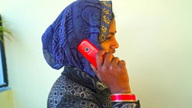 26 March 2021- Khatoo, Jaipur, India. Young Indian lady with red Mobile phone. Blue ornamented lady, covering head with blue saree and calling on mobile.