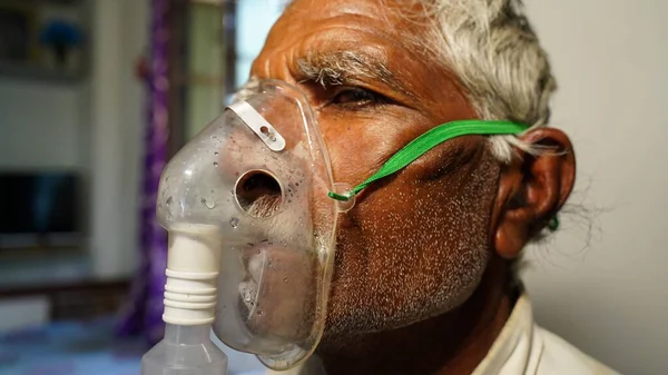 Old Indian man infected with Covid 19 disease. Patient inhaling oxygen wearing mask with liquid Oxygen flow.