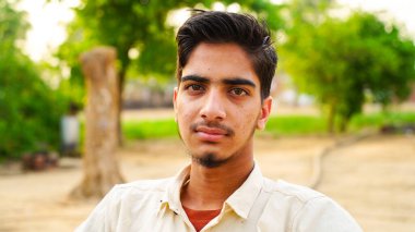 Parkta oturmuş kameraya bakan sağlıklı bir gencin portresi..