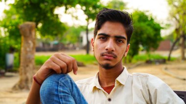 Parkta oturmuş kameraya bakan sağlıklı bir gencin portresi..