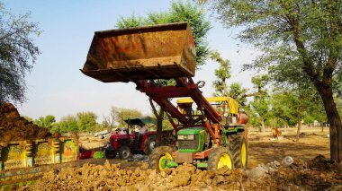 07 Mayıs 2021 - Reengus, Sikar, Hindistan. Loder 'la ağır bir traktör kullanan genç bir Hintli. Çiftçi traktörden organik gübreyi yük vagonunda dolduruyor..
