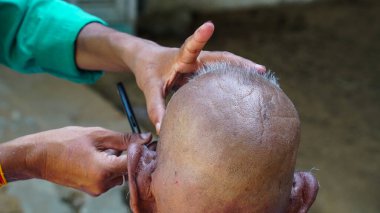 Kimliği belirsiz berber, sokakta oturan Kızılderili 'yi tıraş ediyor. Kırsal Hindistan manzarası.