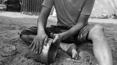 Siyah beyaz atış, kırmızı gömlekli genç adam pirinç tencereyi toprak ve suyla temizlemeye çalışıyor. Saf toprak, tencereleri temizlemek için en iyi bakteridir..