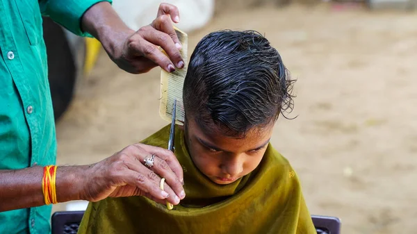 Indian barber working on the village streets in a sunny day. A barber cutting hair of Indian boy during lockdown in India.