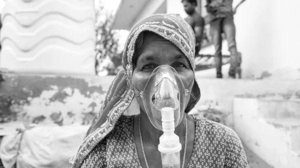 Old Indian woman infected with Covid 19 disease. Patient inhaling oxygen wearing mask with liquid Oxygen flow.