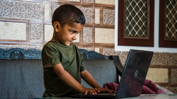 Education at home concept. Indian little cute boy studying using laptop technology.
