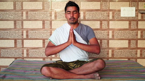 Asian man is doing yoga meditation in the living room at home. He is meditating on floor mat in morning sunshine.