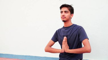 Hintli genç çocuk evde meditasyon yapıyor. Beyaz arka planda yoga yapan Asyalı sevimli çocuğun portresi. Dünya çapında yoga günü konsepti.